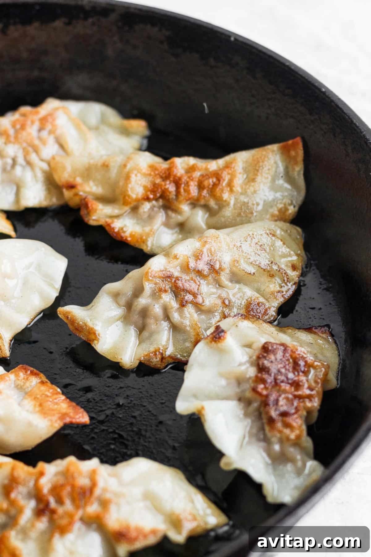 These homemade pork dumplings are packed with savory umami flavors. Make a batch and serve with our amazing sweet dipping sauce that perfectly complements the dumplings. Closeup of pork dumplings being expertly pan-fried in a hot cast iron skillet