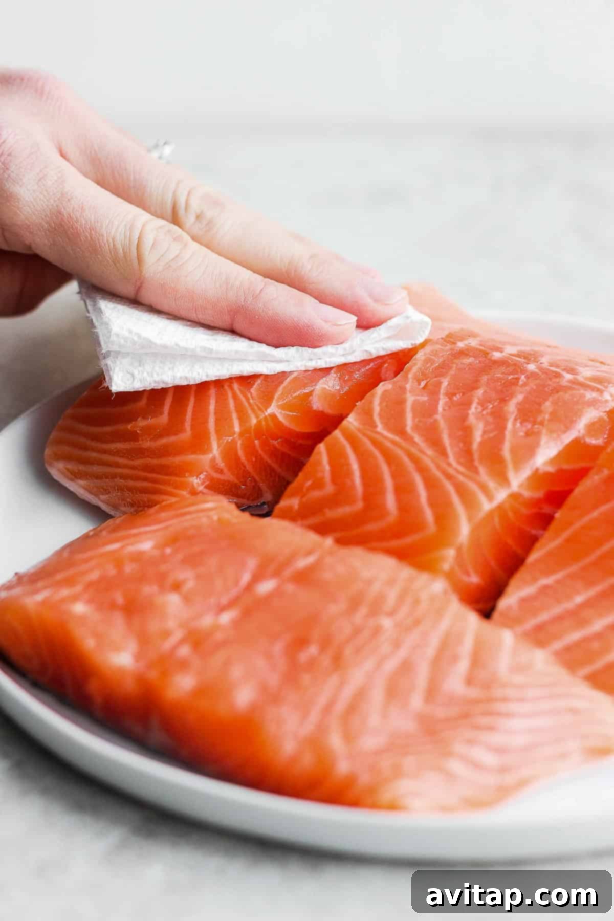 Patting raw salmon with a paper towel to remove moisture for crispy skin.