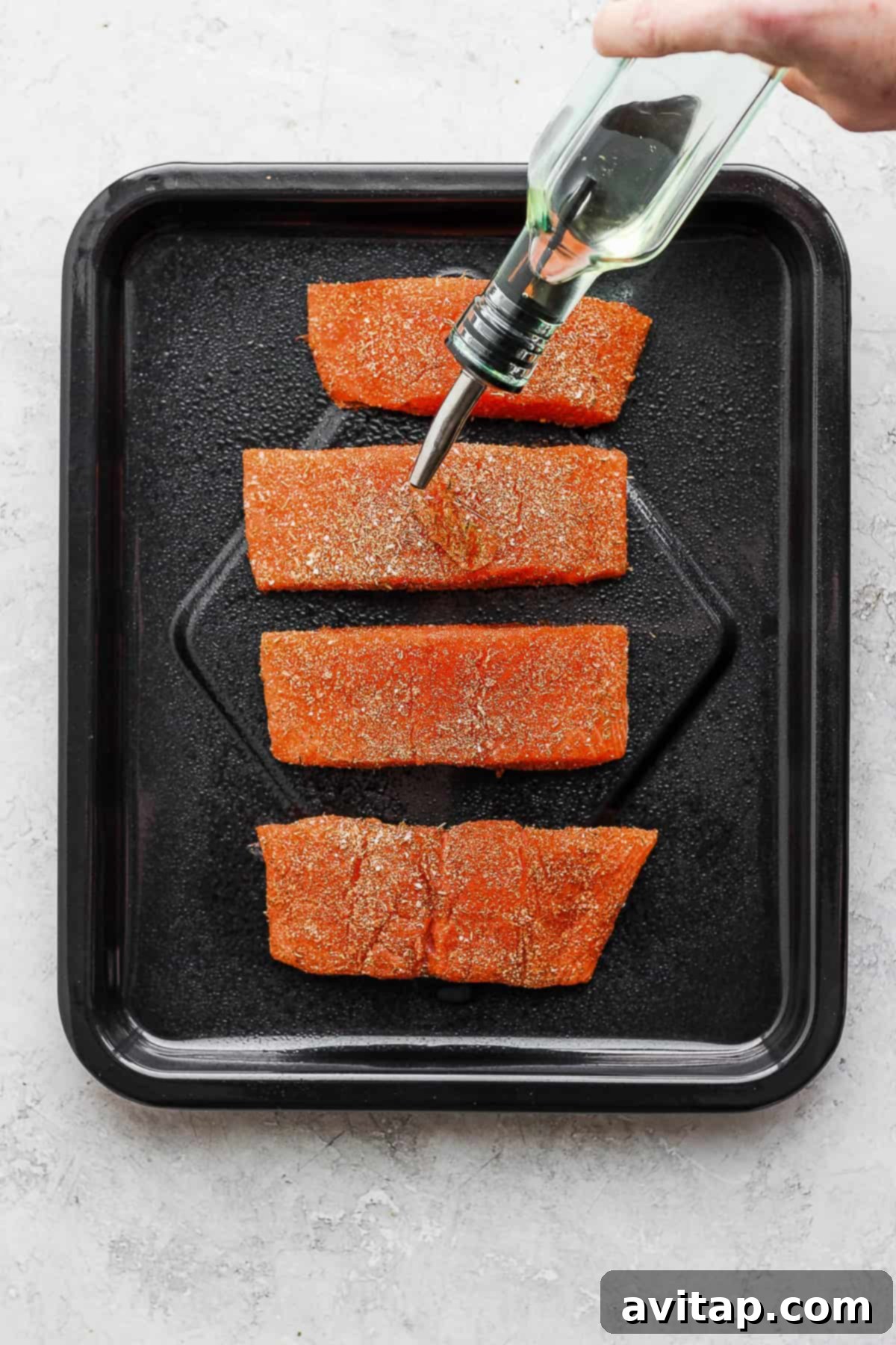 Drizzling olive oil over seasoned salmon fillets in the air fryer basket.