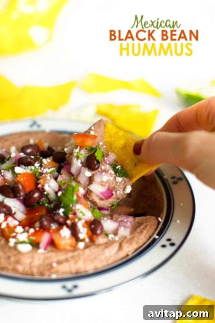 A vibrant bowl of Mexican Black Bean Hummus, garnished with fresh cilantro and a sprinkle of cotija cheese, ready to be served with tortilla chips for a healthy game day appetizer.