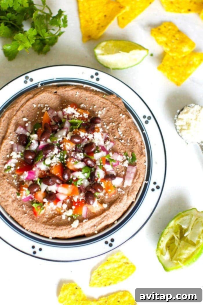 A beautifully presented bowl of Mexican Black Bean Hummus, generously topped with vibrant diced tomatoes, fresh cilantro, and crumbled cotija cheese, perfect for a festive and healthy snack.