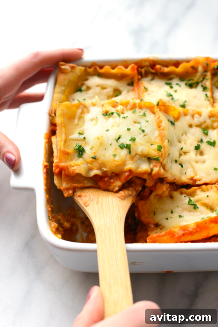 A serving spoon lifting a generous portion of sweet potato lasagna, highlighting its rich, saucy, and cheesy texture, ready to be served.