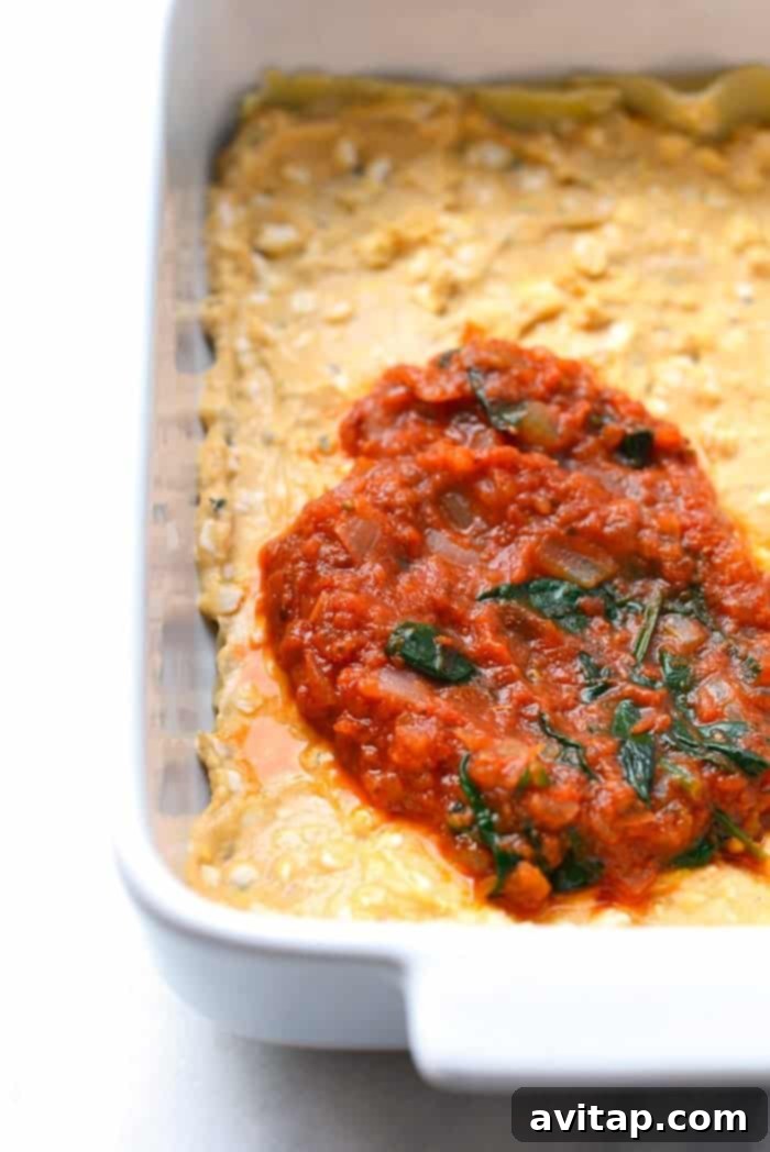 Rich tomato and spinach sauce being generously spread over a layer of lasagna noodles in a baking dish, preparing for the next layer of deliciousness.