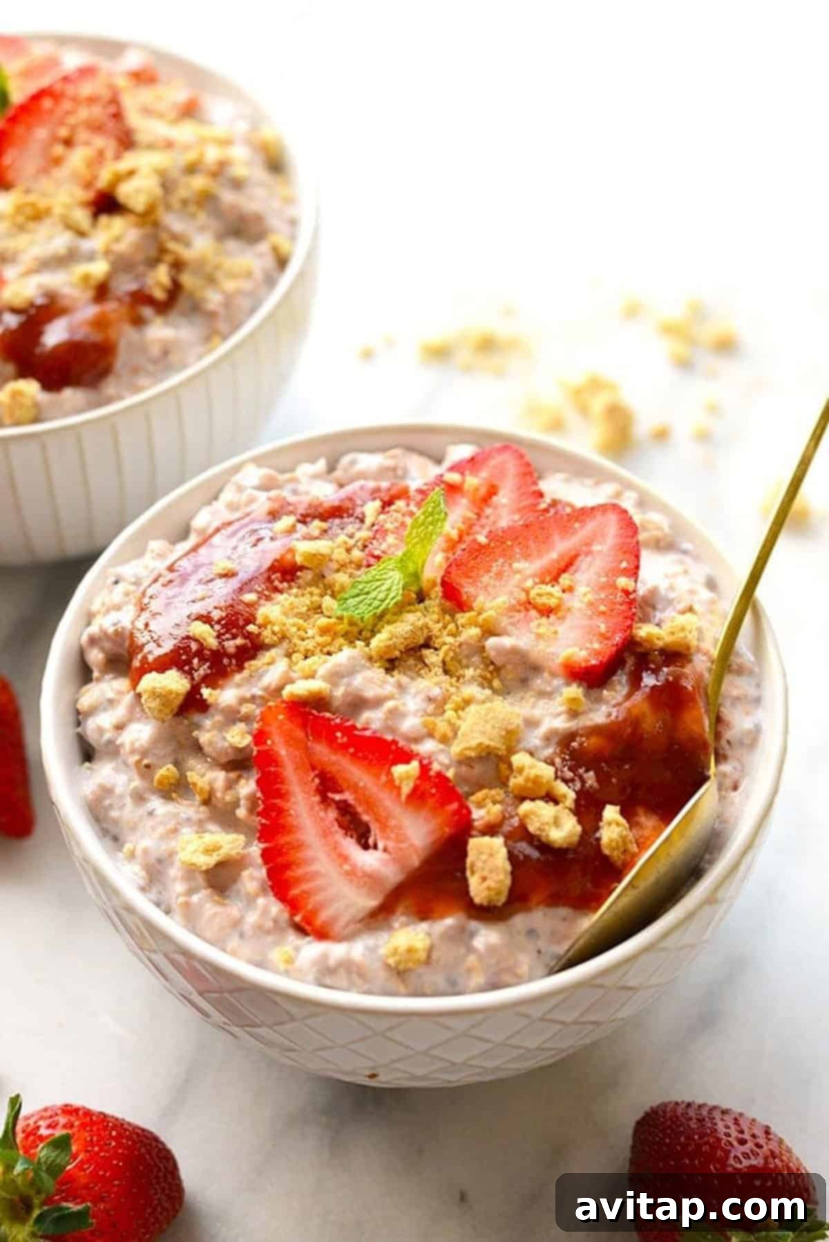 A bowl of creamy strawberry cheesecake overnight oats, topped with fresh strawberries and graham cracker crumbles.