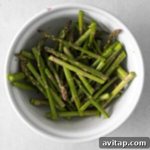 Seasoned asparagus in a bowl, coated with lemon juice, olive oil, salt, and pepper.