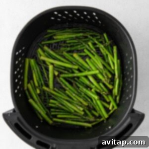 Fresh asparagus spears arranged inside an air fryer basket, ready to be cooked.