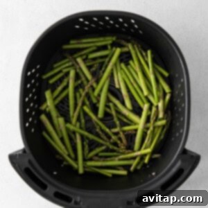 Crispy asparagus spears cooking inside the air fryer, showing perfect doneness.