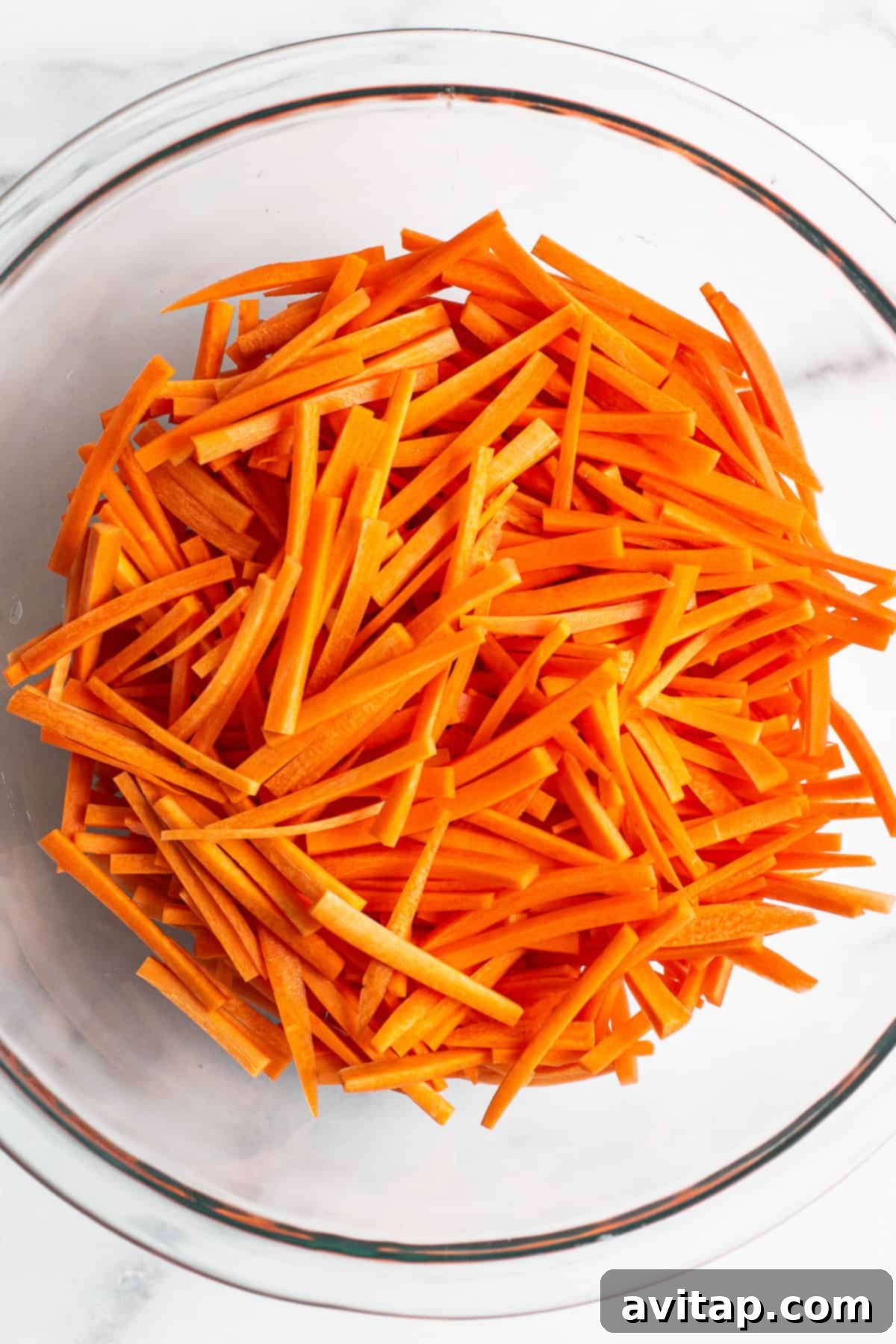 Freshly julienned carrots in a large mixing bowl, ready for French Carrot Salad preparation.