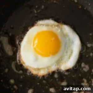An egg being fried in a nonstick pan, with the butter sizzling around it.