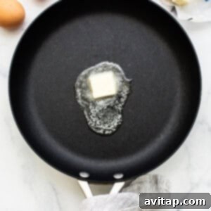 A pad of butter melting and sizzling in a hot nonstick pan.