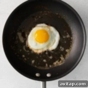 A fried egg cooking in a pan, with the white solidifying around the yolk.