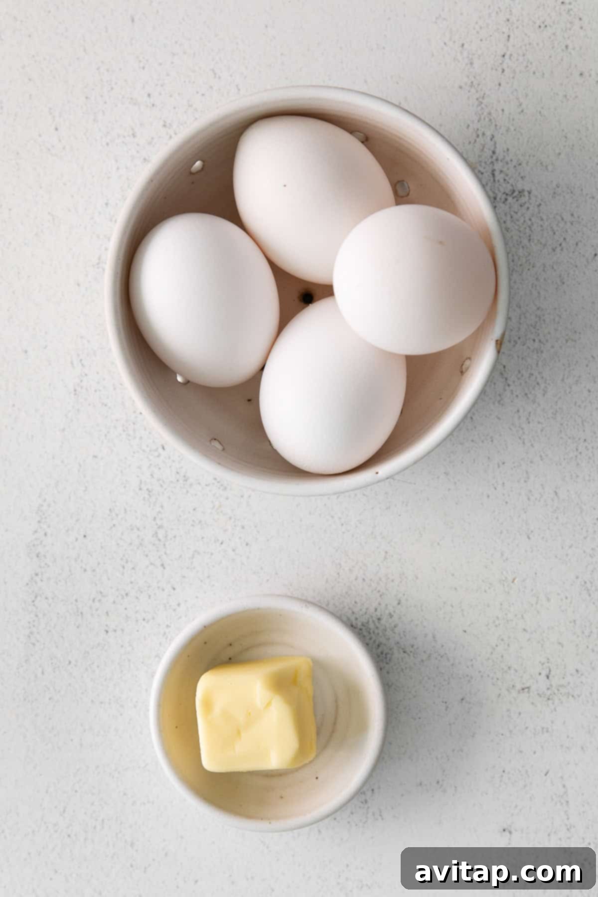 Four large fresh eggs resting in a white ceramic bowl, ready for frying.