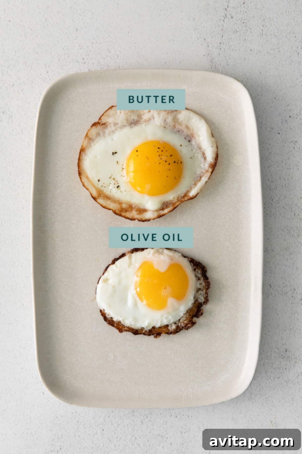 An egg fried in butter with minimal browning and an egg fried in oil with crispy, lacy edges, presented side-by-side on a white plate.