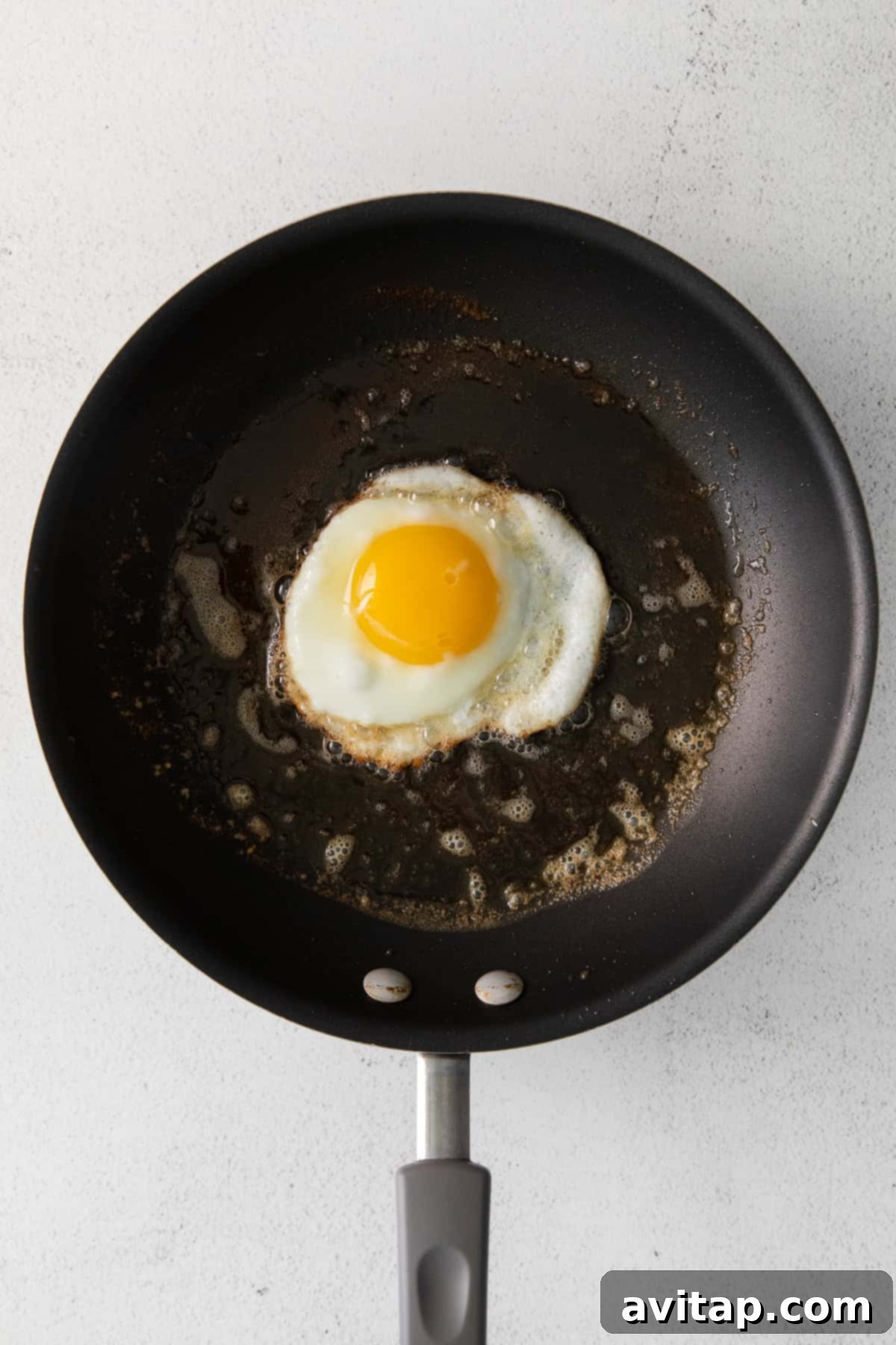 A close-up of an egg sizzling in melted butter in a nonstick pan, with the white just beginning to set.