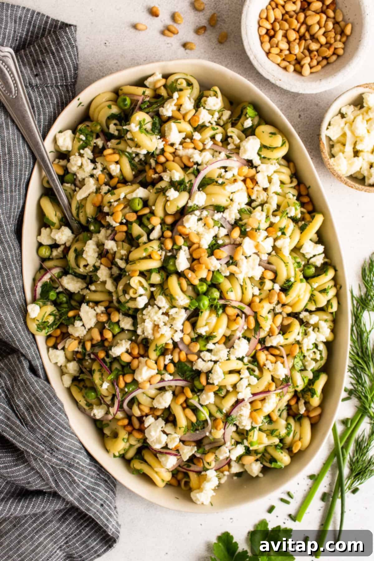 Large bowl filled with vibrant lemon pasta salad, garnished with fresh herbs, feta, and pine nuts.