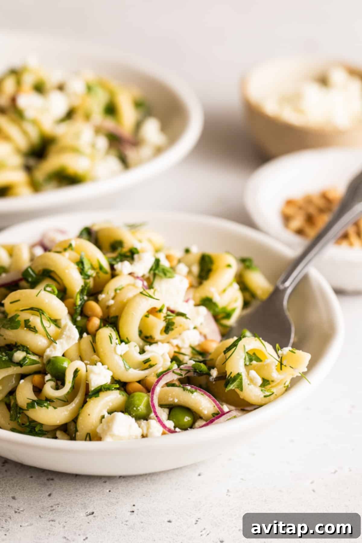 Close-up of a beautifully presented bowl of lemon pasta salad, garnished with fresh herbs, crumbled feta, and toasted pine nuts.
