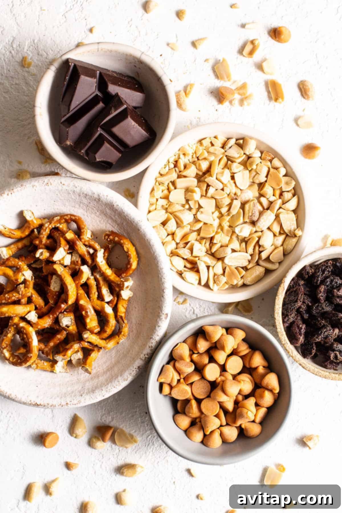 Various kitchen sink cookie ingredients laid out in separate bowls, including butter, sugar, oats, and assorted mix-ins like chocolate chips and nuts.