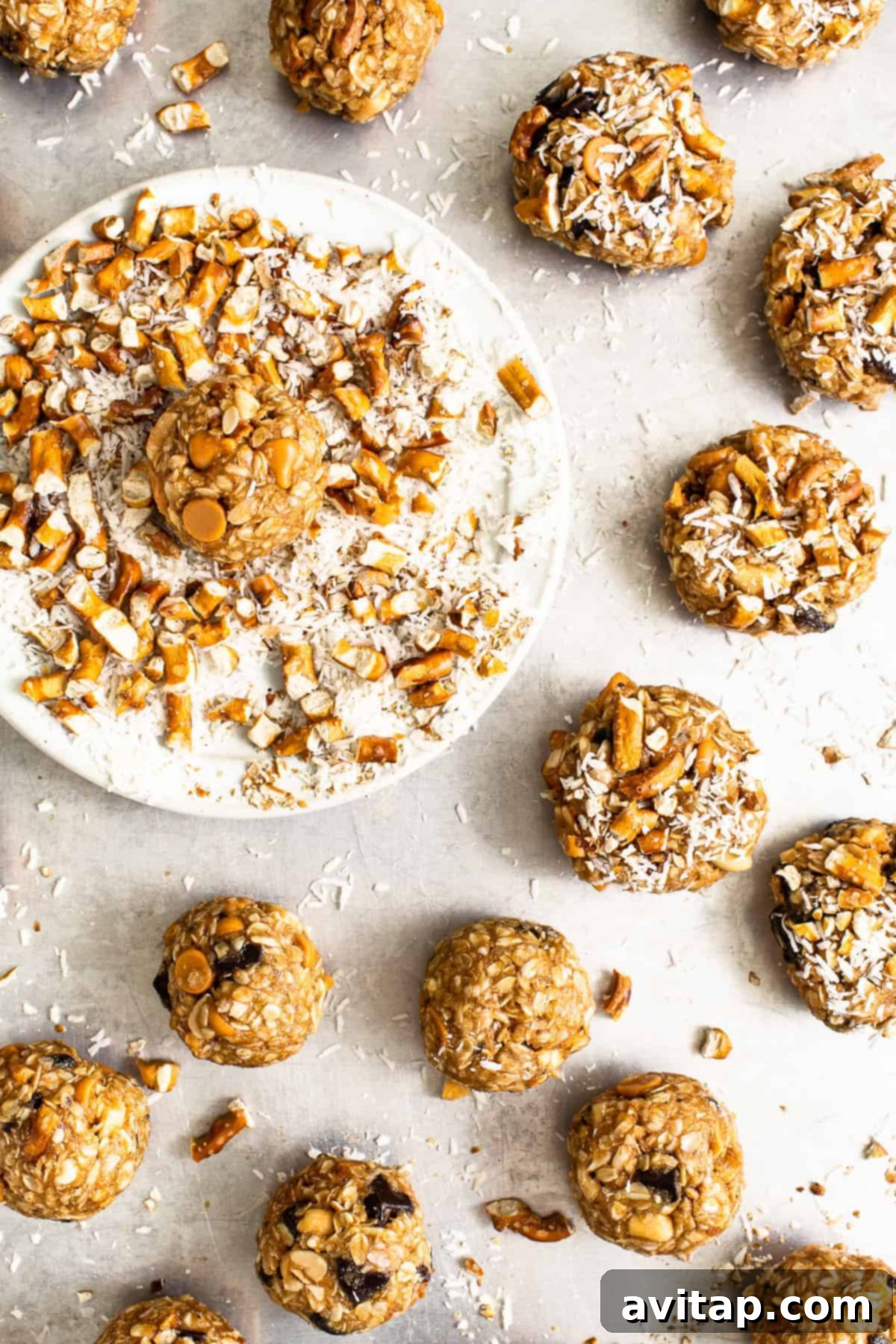 Cookie dough balls rolled in extra shredded coconut and crushed pretzels, arranged on a plate and ready for baking.