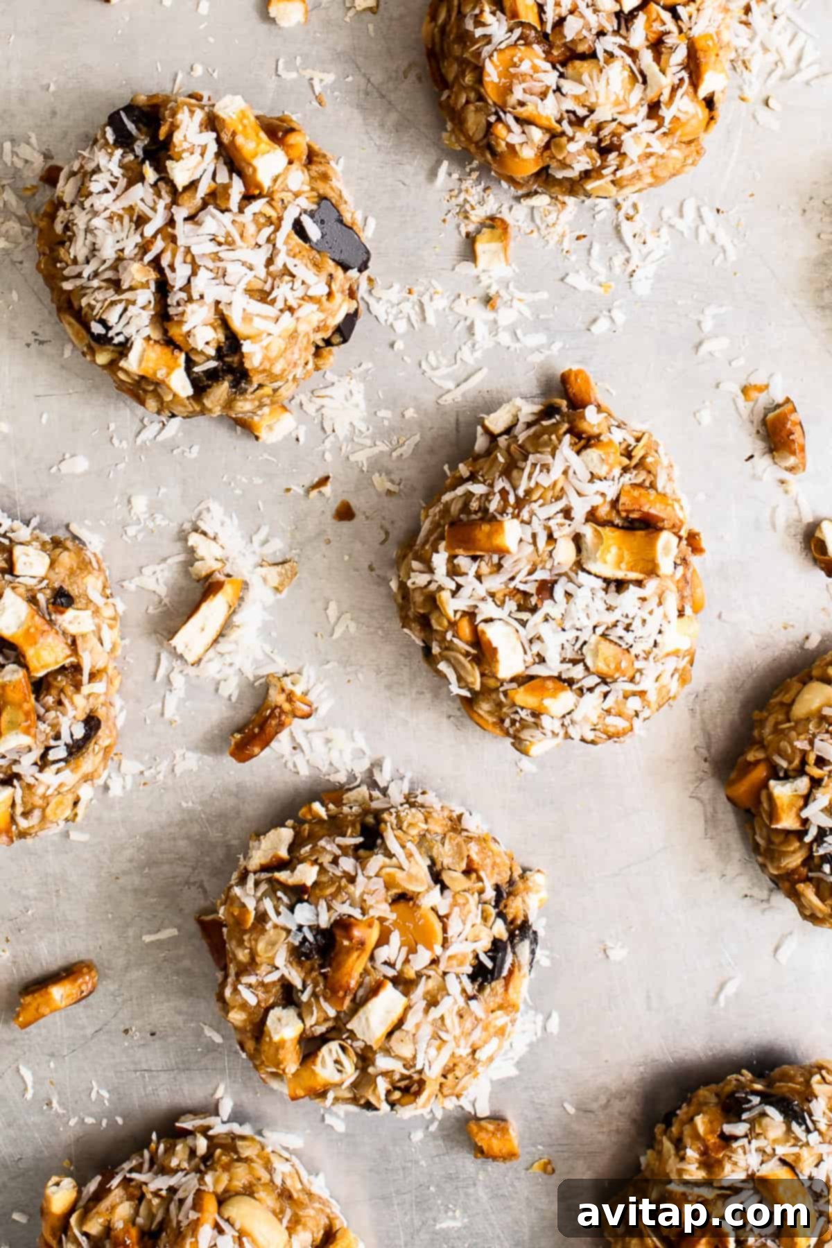 Baked kitchen sink cookies on a baking sheet, some topped with coconut flakes, ready to be transferred to a cooling rack.