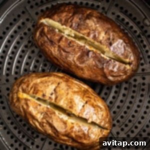 Two baked potatoes cooking in an air fryer basket.