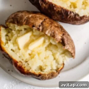 Two baked potatoes with butter on a plate, ready to be served.