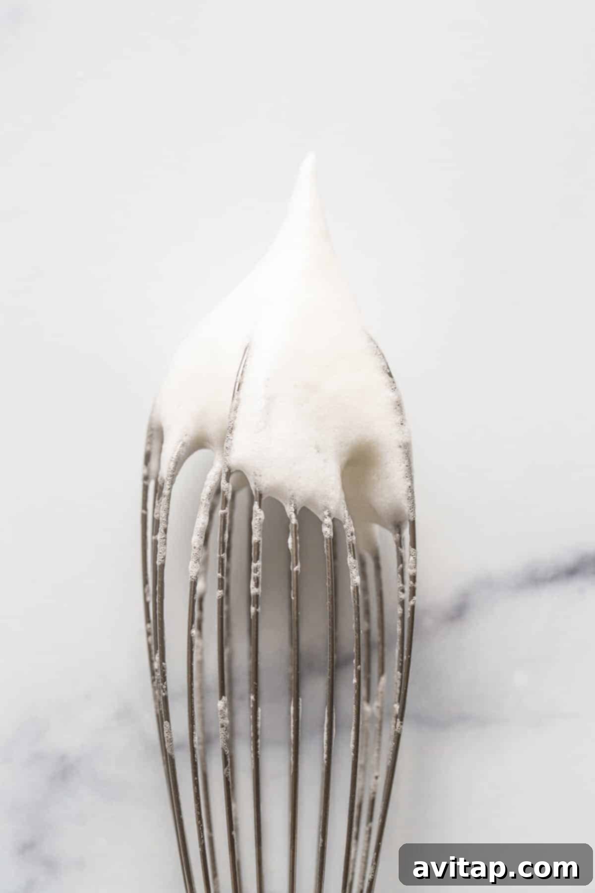 Stiff peaks of egg whites on a whisk, perfectly prepared to be folded into pancake batter
