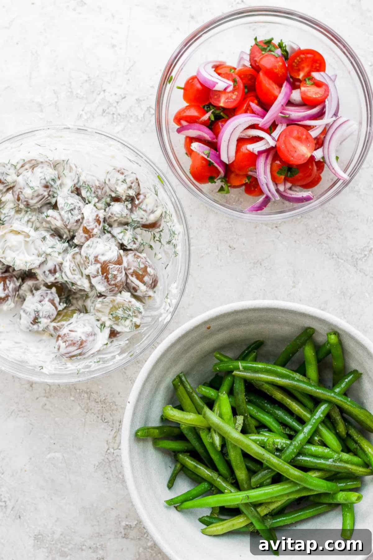 Various fresh ingredients for a Nicoise Salad, including tomatoes, potatoes, and green beans, arranged in separate bowls.