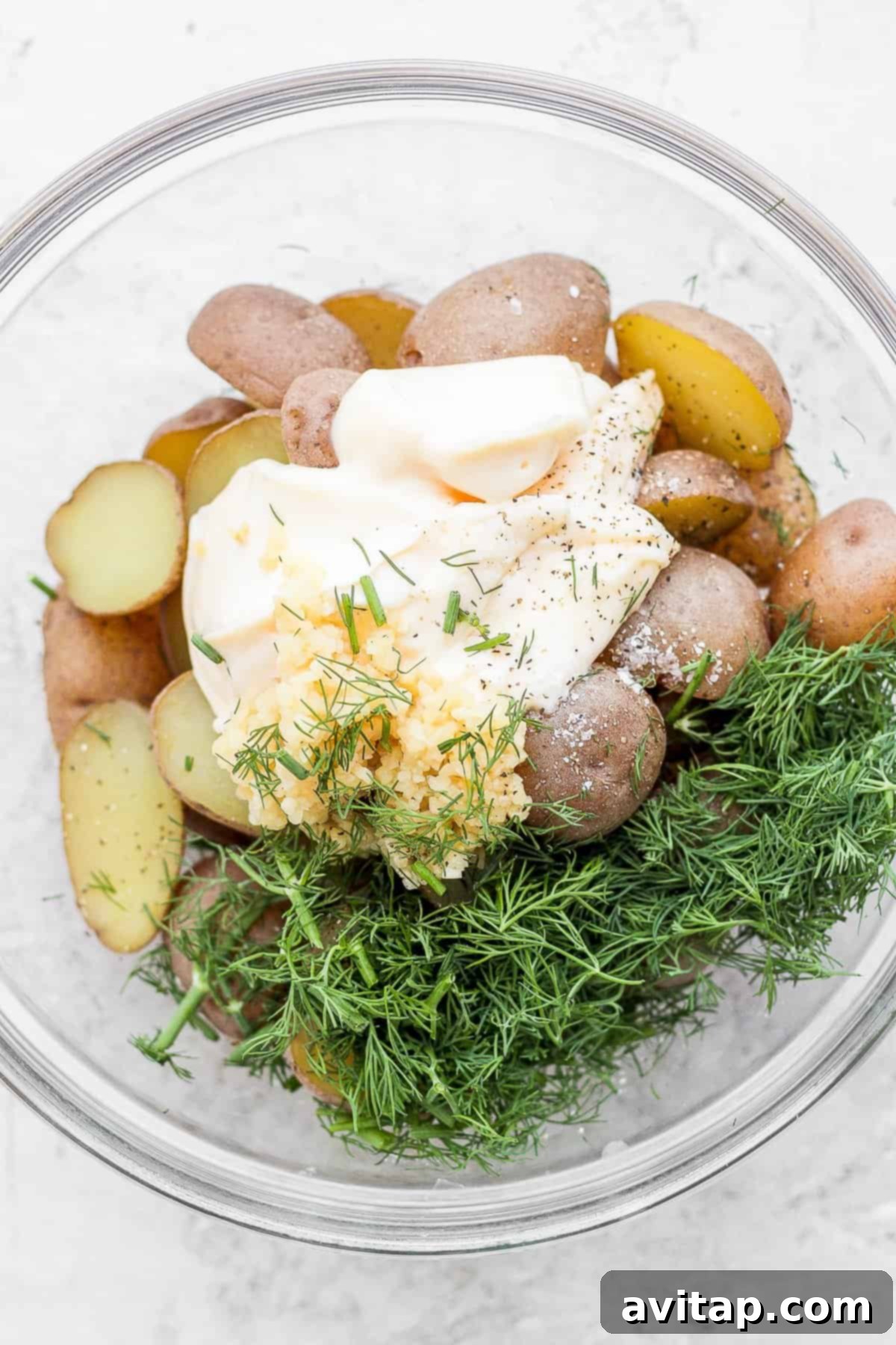 Cooked potatoes in a bowl, mixed with mayonnaise, minced garlic, and fresh dill.