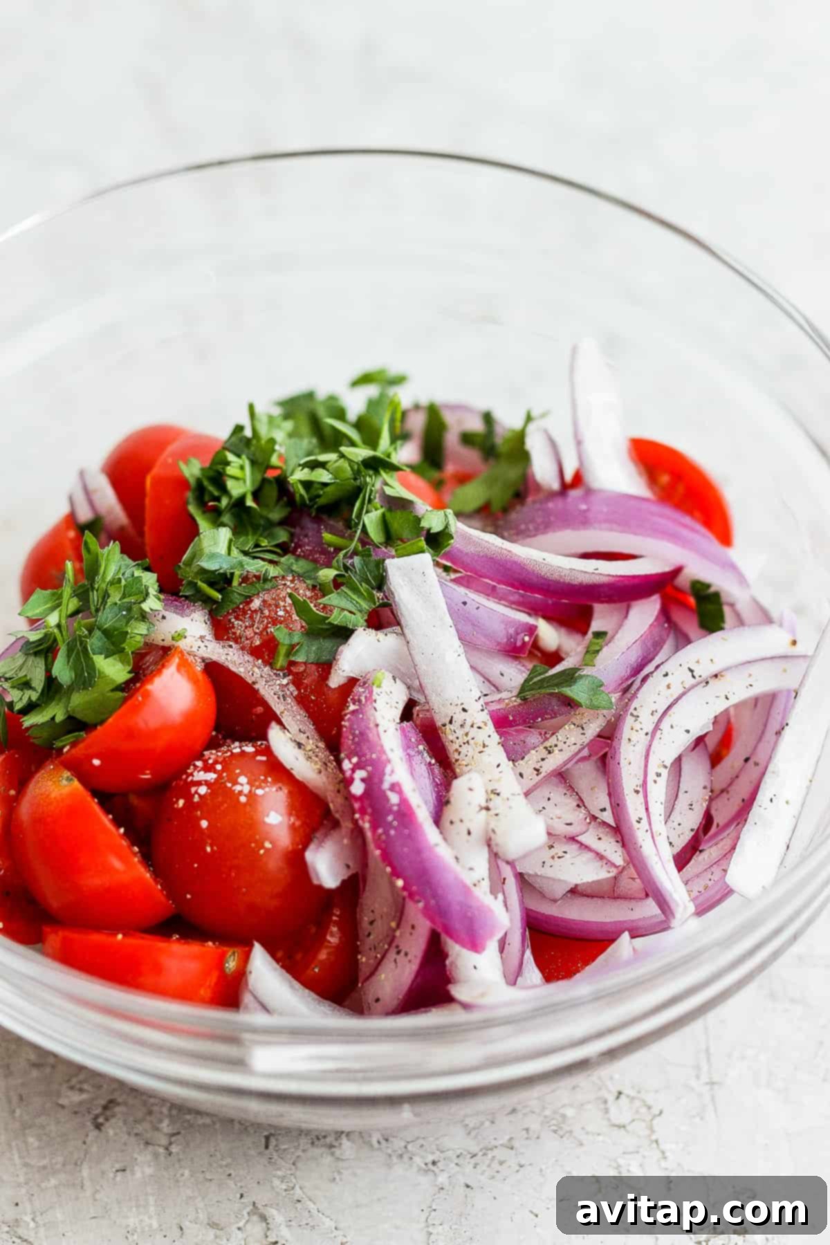 Halved cherry tomatoes, thinly sliced red onion, and fresh parsley marinating in a bowl.