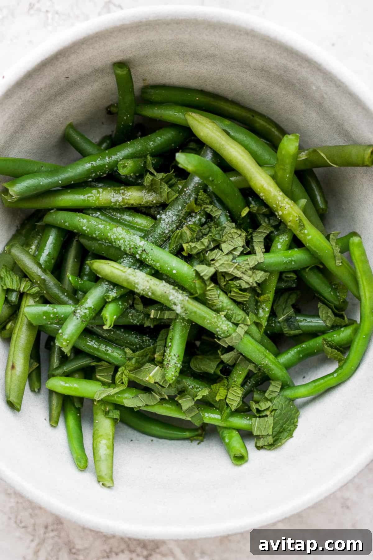 Blanched green beans tossed with fresh mint in a bowl, ready to be added to the salad.