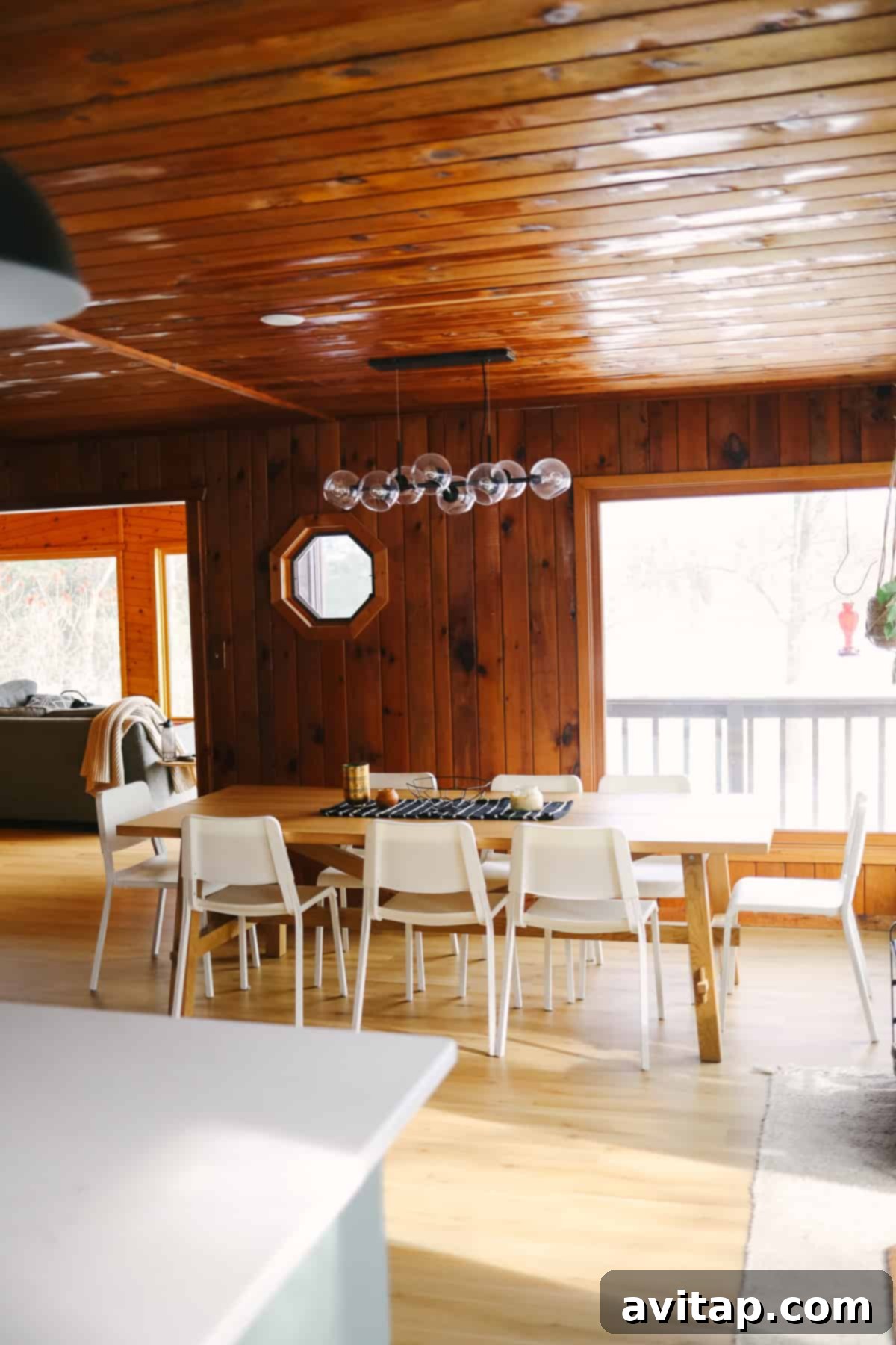 A large IKEA Mockelby dining table surrounded by IKEA Janinge chairs, illuminated by a modern West Elm fixture, in a Scandinavian Modern cabin setting.