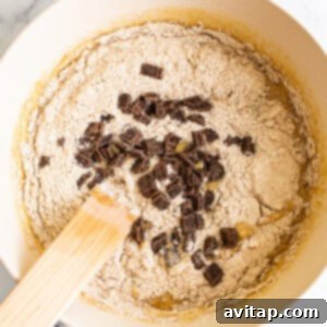 Mixing banana bread batter with chocolate chips in a bowl using a wooden spoon.