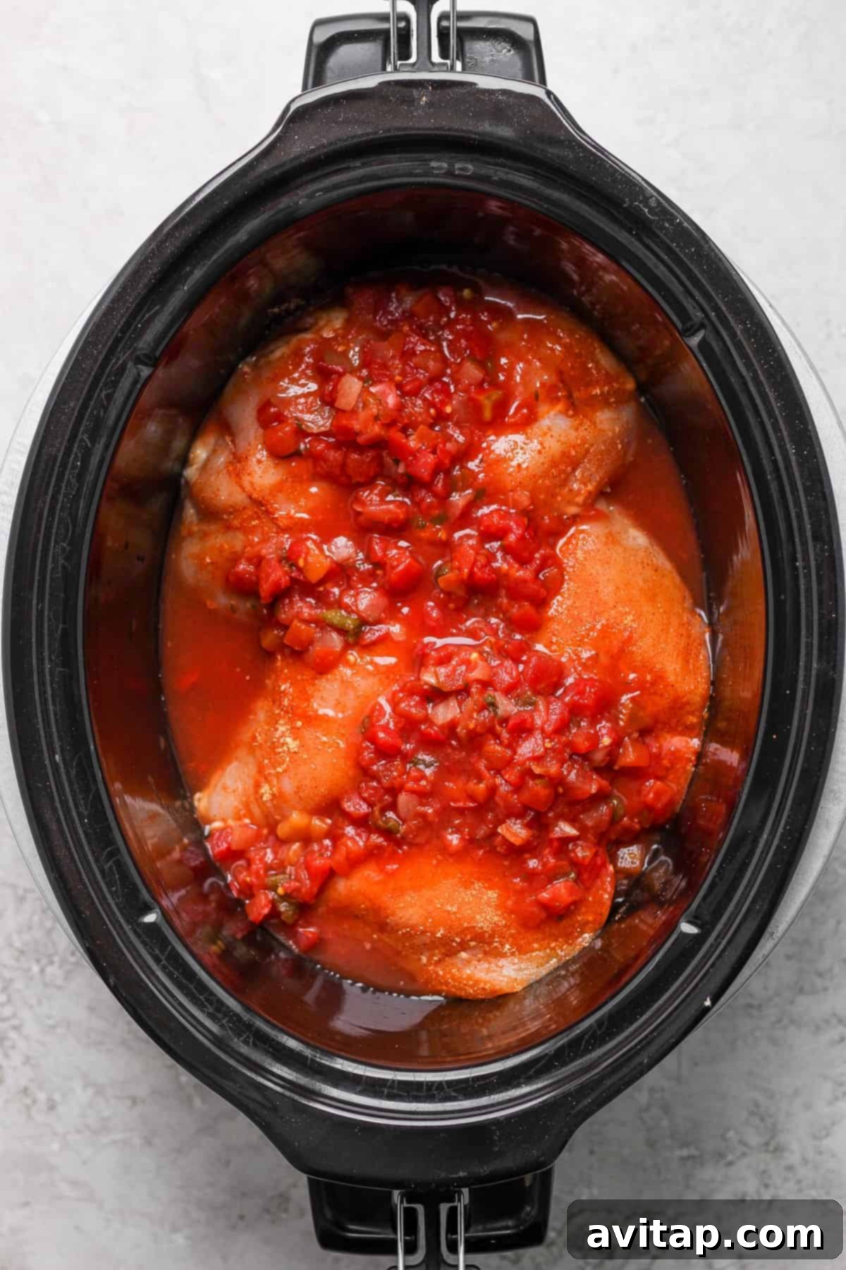 Chicken breast generously covered in salsa, simmering in a slow cooker.