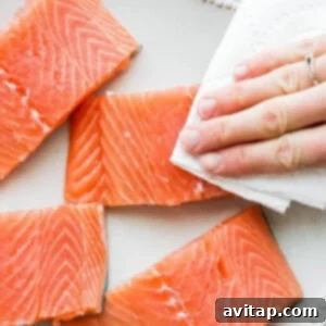 A person is holding a piece of salmon on a plate.