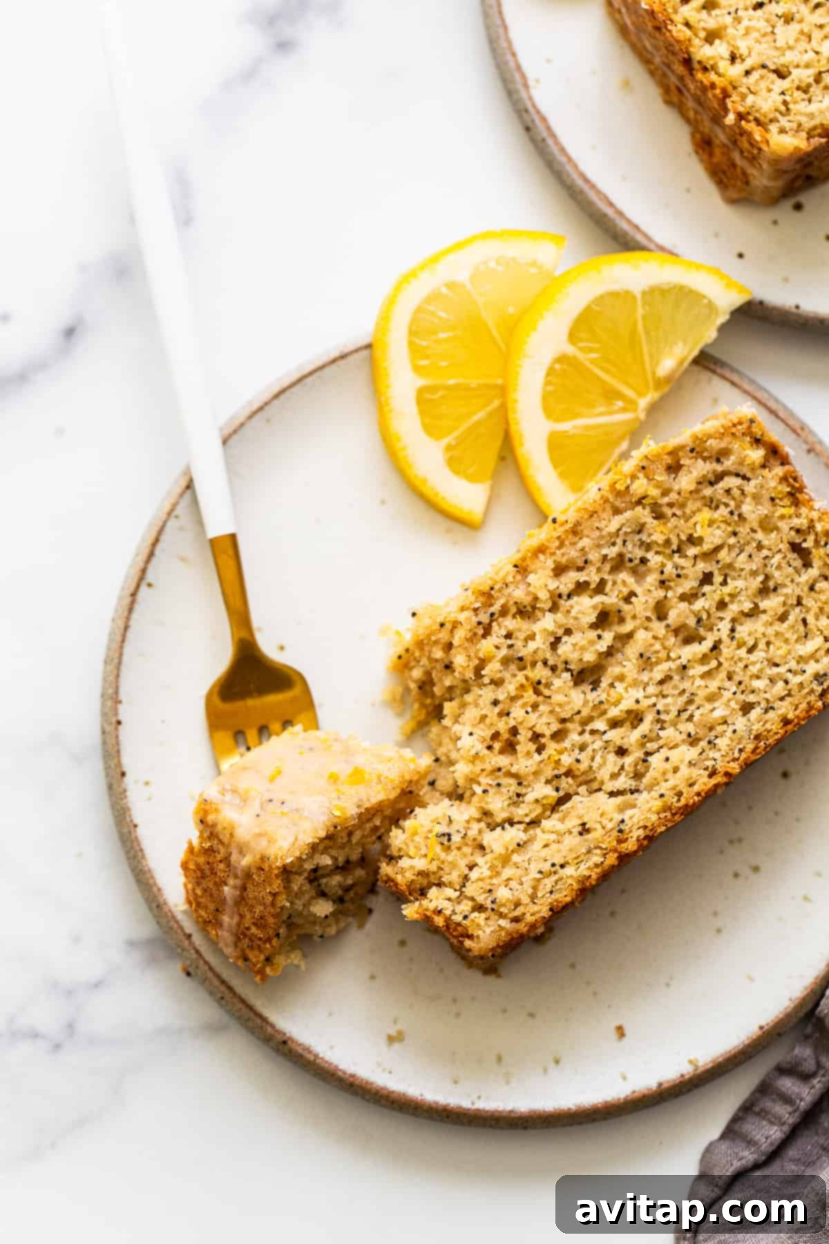 A perfectly baked slice of lemon poppy seed bread on a white plate, showcasing its fluffy texture and golden crust, topped with a glistening lemon glaze.