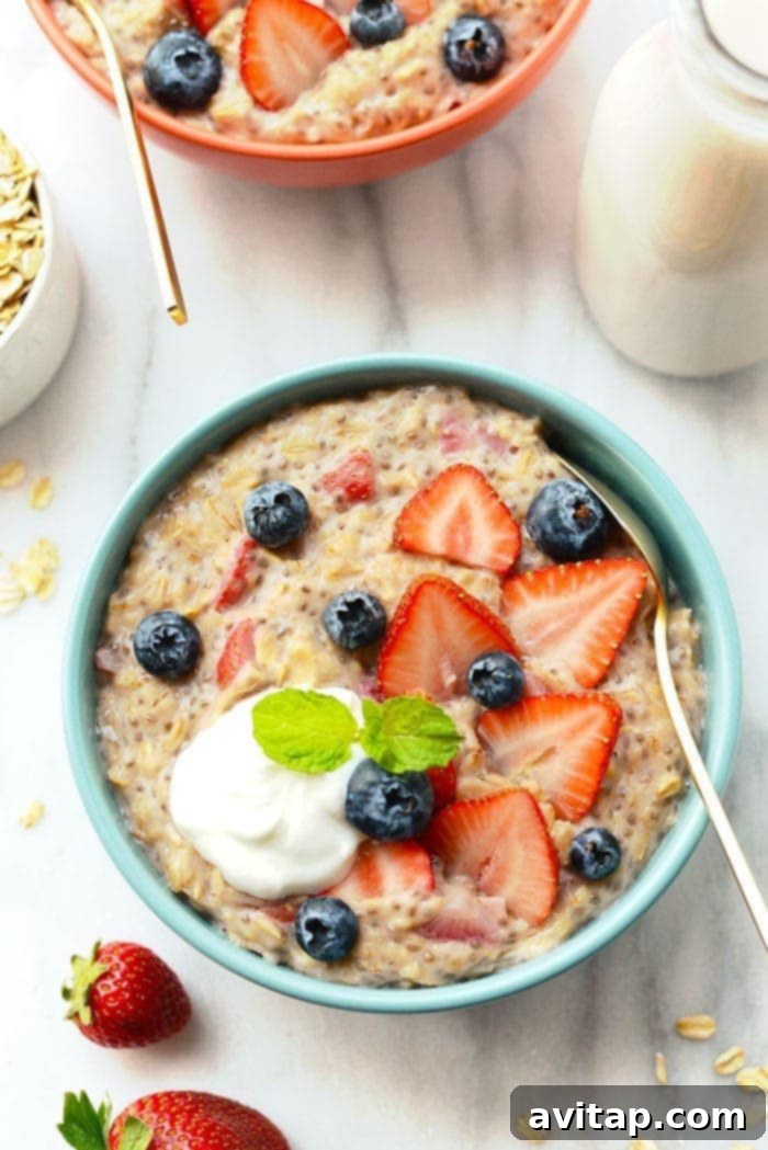 A bowl of freshly made Strawberries and Cream Oatmeal, topped with sliced strawberries and a drizzle of cream, with a spoon ready to dig in. Served on a light wooden surface.