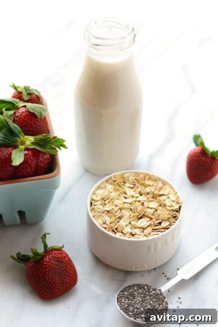 A selection of fresh ingredients for Strawberries and Cream Oatmeal, including rolled oats, fresh strawberries, a banana, chia seeds, and almond milk, neatly arranged on a countertop.