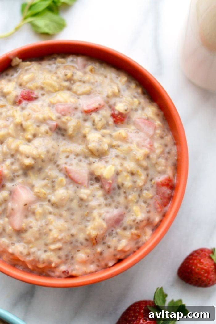A close-up shot of a bowl of Strawberries and Cream Oatmeal, showcasing the thick, creamy texture and generous chunks of fresh strawberries, garnished with a few whole berries.