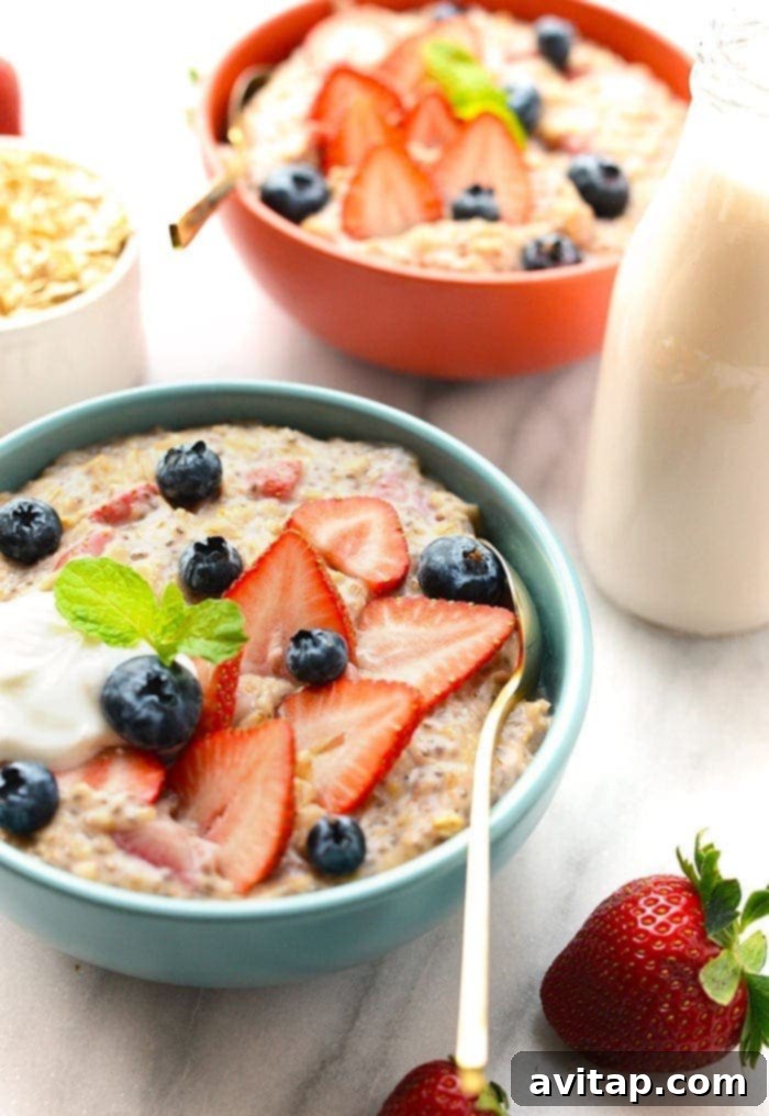 A beautifully arranged bowl of Strawberries and Cream Oatmeal, garnished with a generous amount of fresh strawberries, blueberries, a sprinkle of chia seeds, and a few almond slices, ready to be enjoyed.