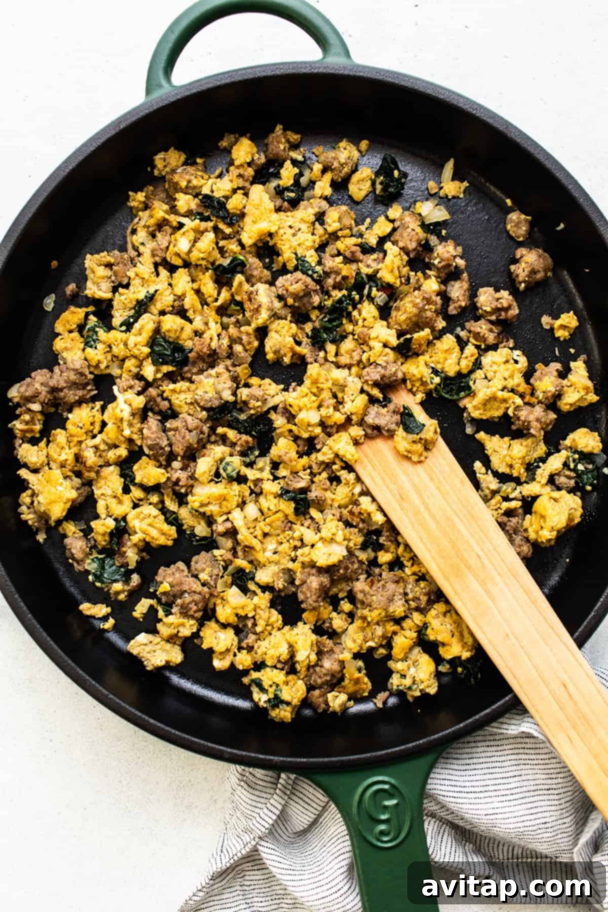 Prepping the flavorful filling for your breakfast quesadillas. Fresh ingredients for breakfast quesadillas: scrambled eggs, savory breakfast sausage, and vibrant kale sautéed in a cast iron skillet.
