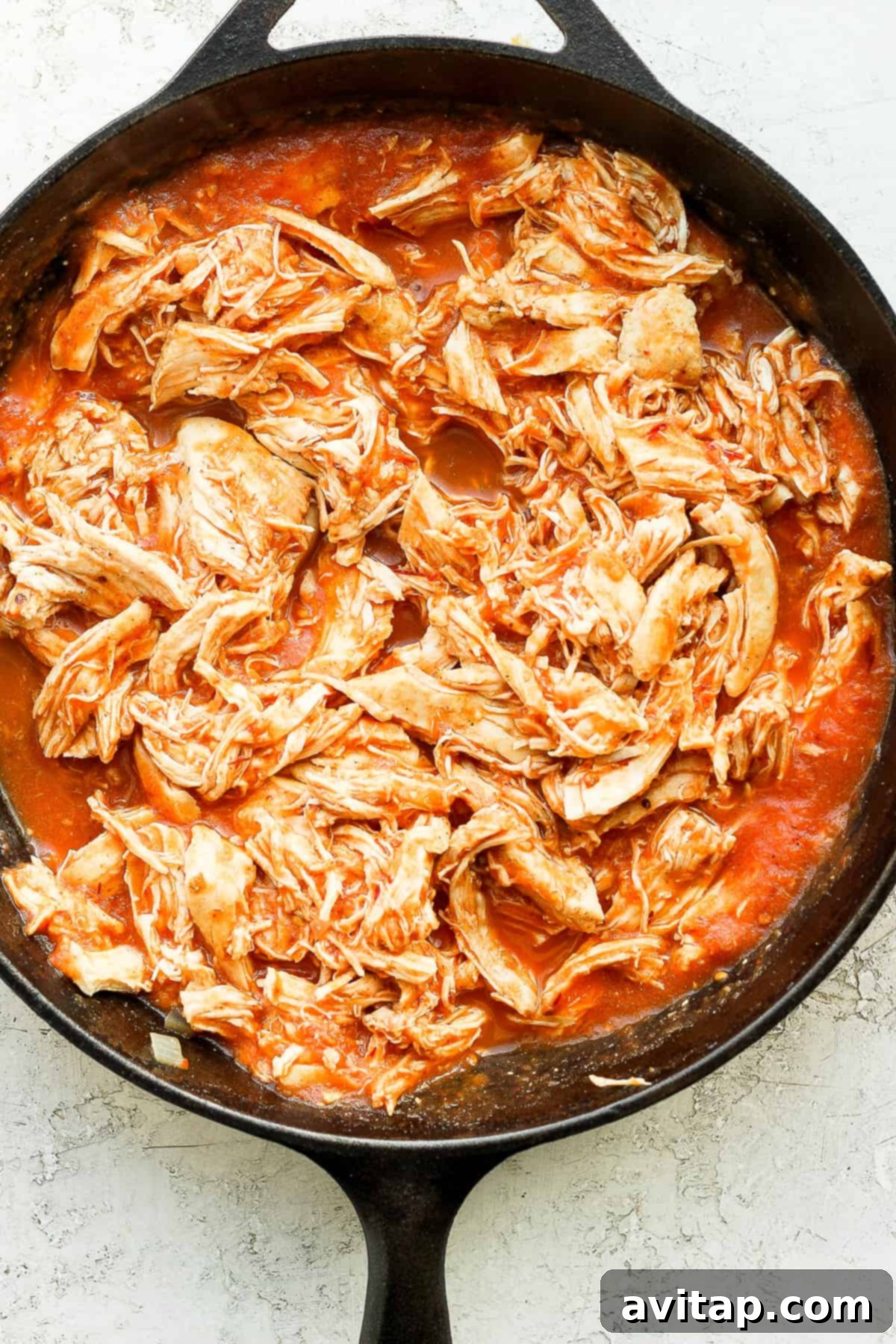 Shredded chicken generously coated in the rich, red tinga sauce in a cast iron skillet.