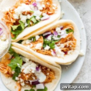 Three delicious chicken tinga tacos on a white plate, garnished with fresh toppings.