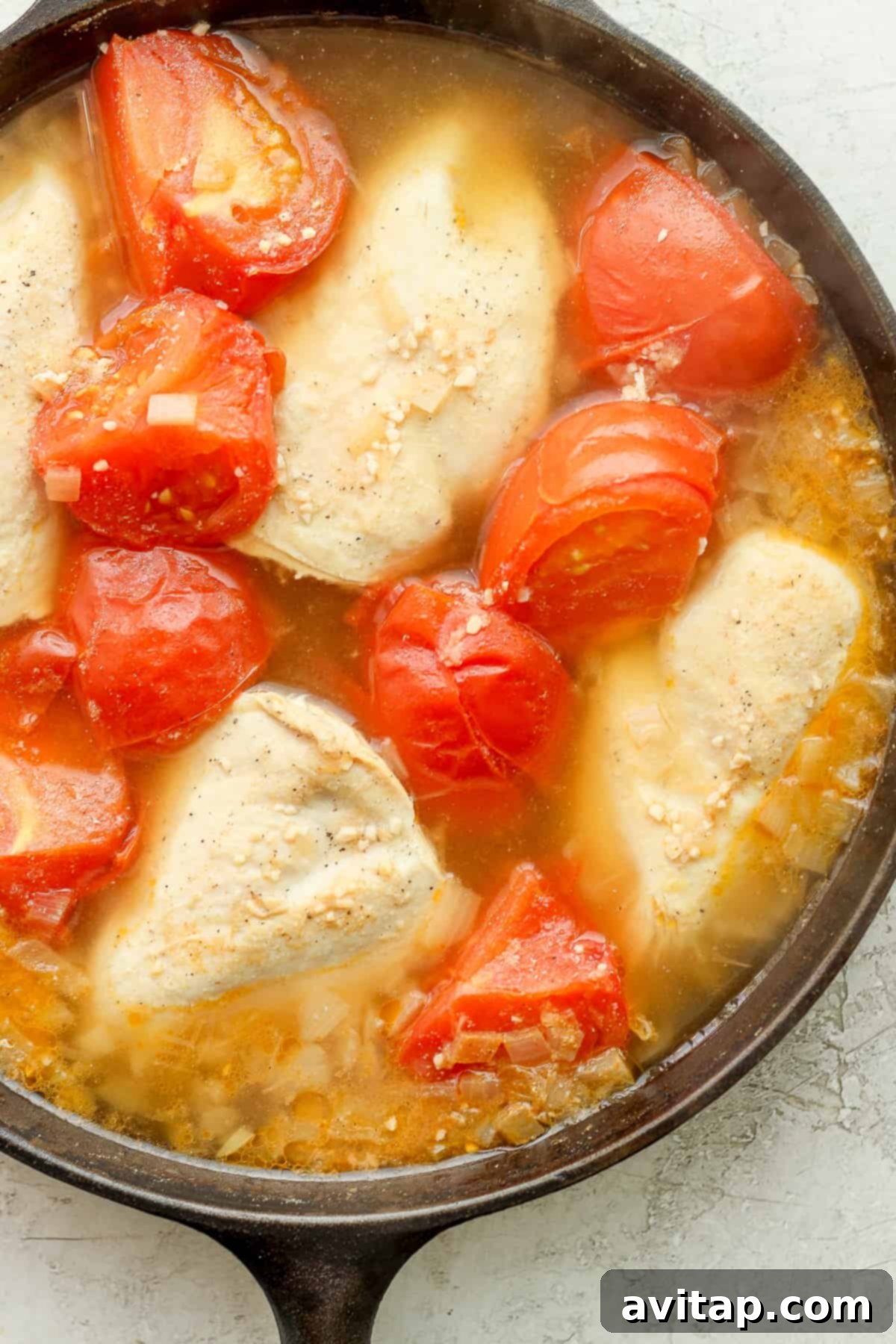 Chicken and quartered tomatoes simmering in a skillet, absorbing rich flavors.