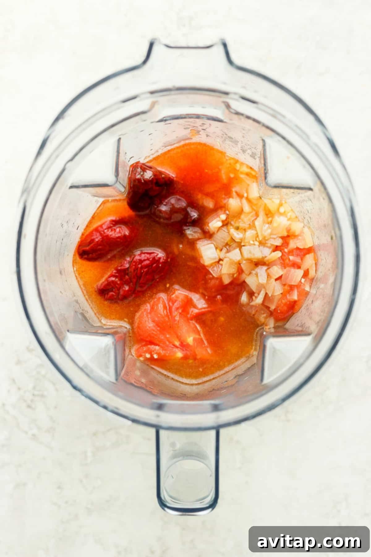 Carefully selected tinga ingredients, including peeled tomatoes, onions, chipotle peppers, and broth, ready for blending.
