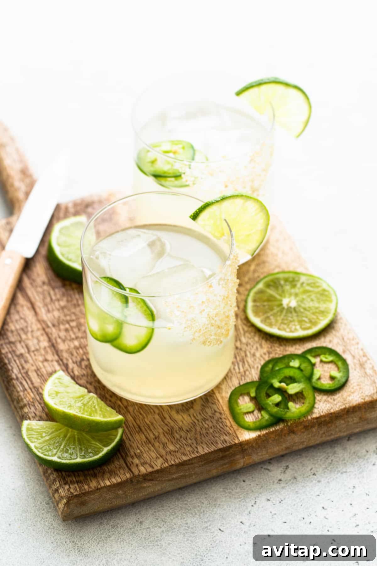 Two spicy mezcal margaritas in elegant glasses, garnished with lime and jalapeño slices.