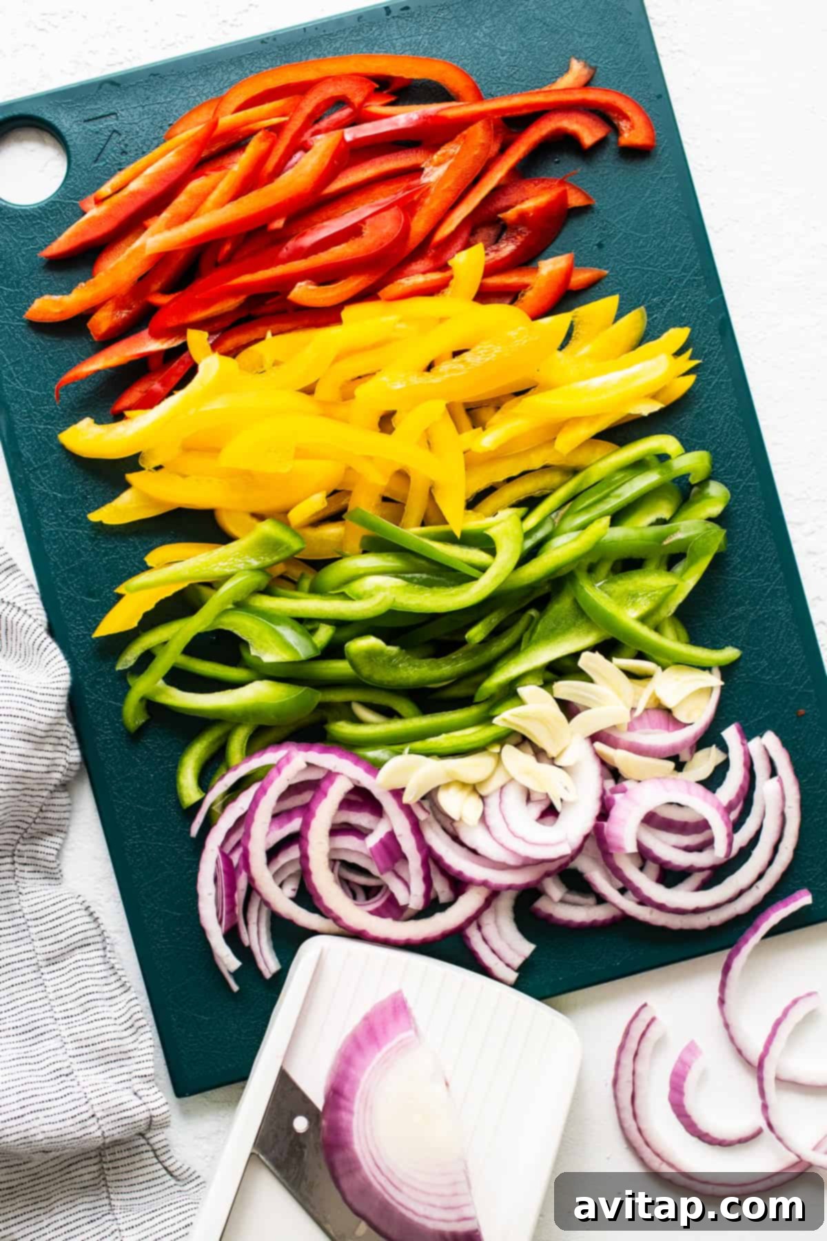 Freshly sliced bell peppers and onions arranged on a wooden cutting board, ready for cooking.