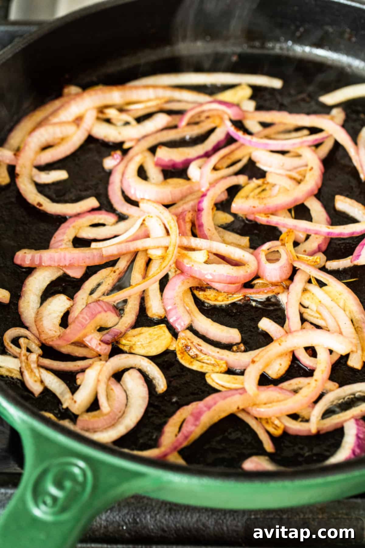 Close-up shot of thinly sliced red onions sizzling and caramelizing in a hot skillet with oil.