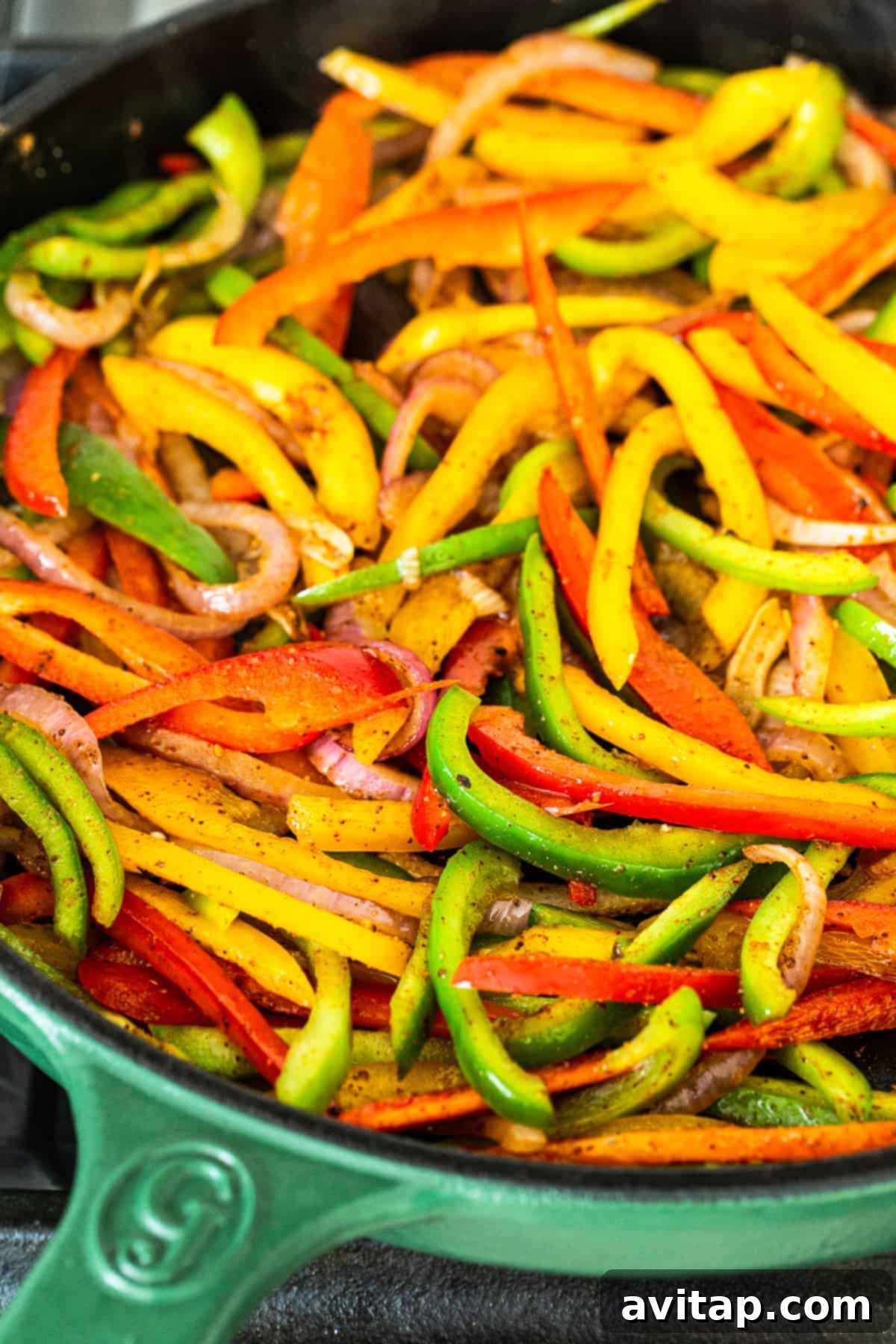 Colorful bell peppers and onions being stir-fried in a hot cast iron pan, creating a vibrant and appetizing dish.