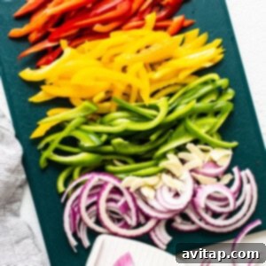Sliced peppers and onions on a cutting board, neatly prepared for cooking.