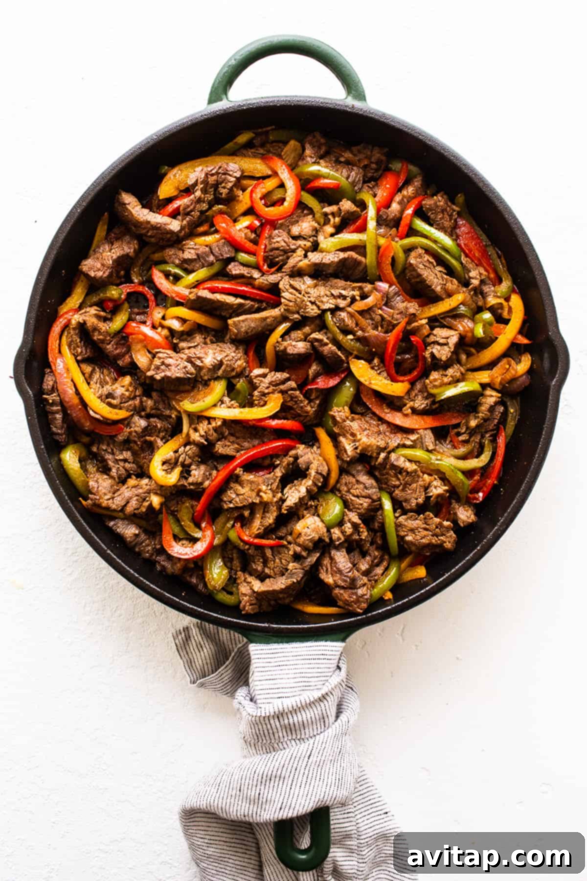 Sizzling steak fajitas and colorful fajita vegetables actively cooking in a cast iron skillet, emitting steam and aromas, ready to be served hot.